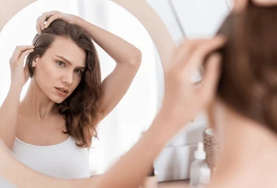 Woman noticing hair thinning near frontal hairline while looking in mirror