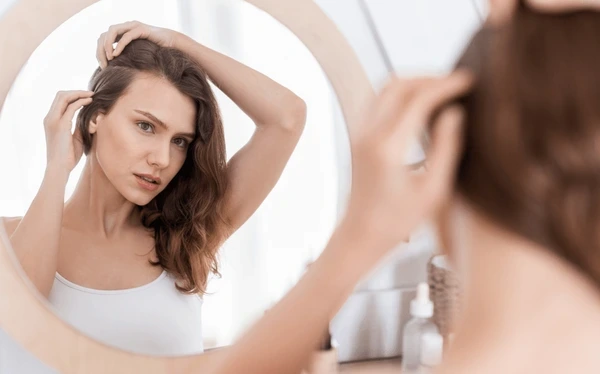 Woman noticing hair thinning near frontal hairline while looking in mirror