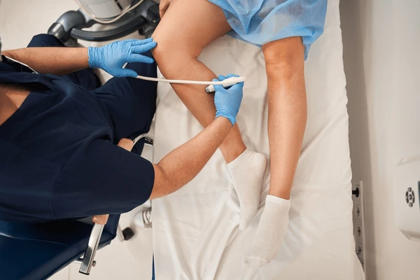 Doctor performing leg ultrasound to evaluate arterial stiffness vs venous insufficiency